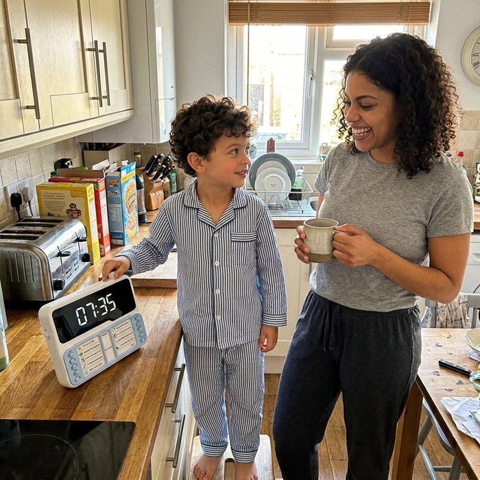 Un garçon en pyjama pose la main sur son minuteur Hopinou, sa maman sourit